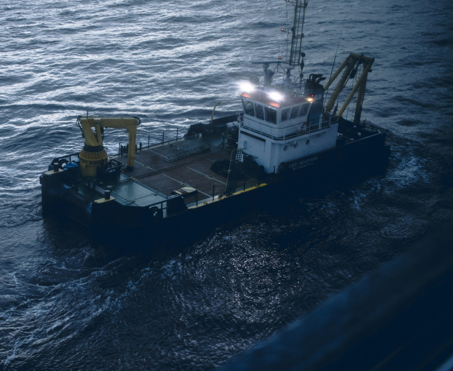 Four people seated around a conference table in a glass-walled office with large windows overlooking a cityscape.