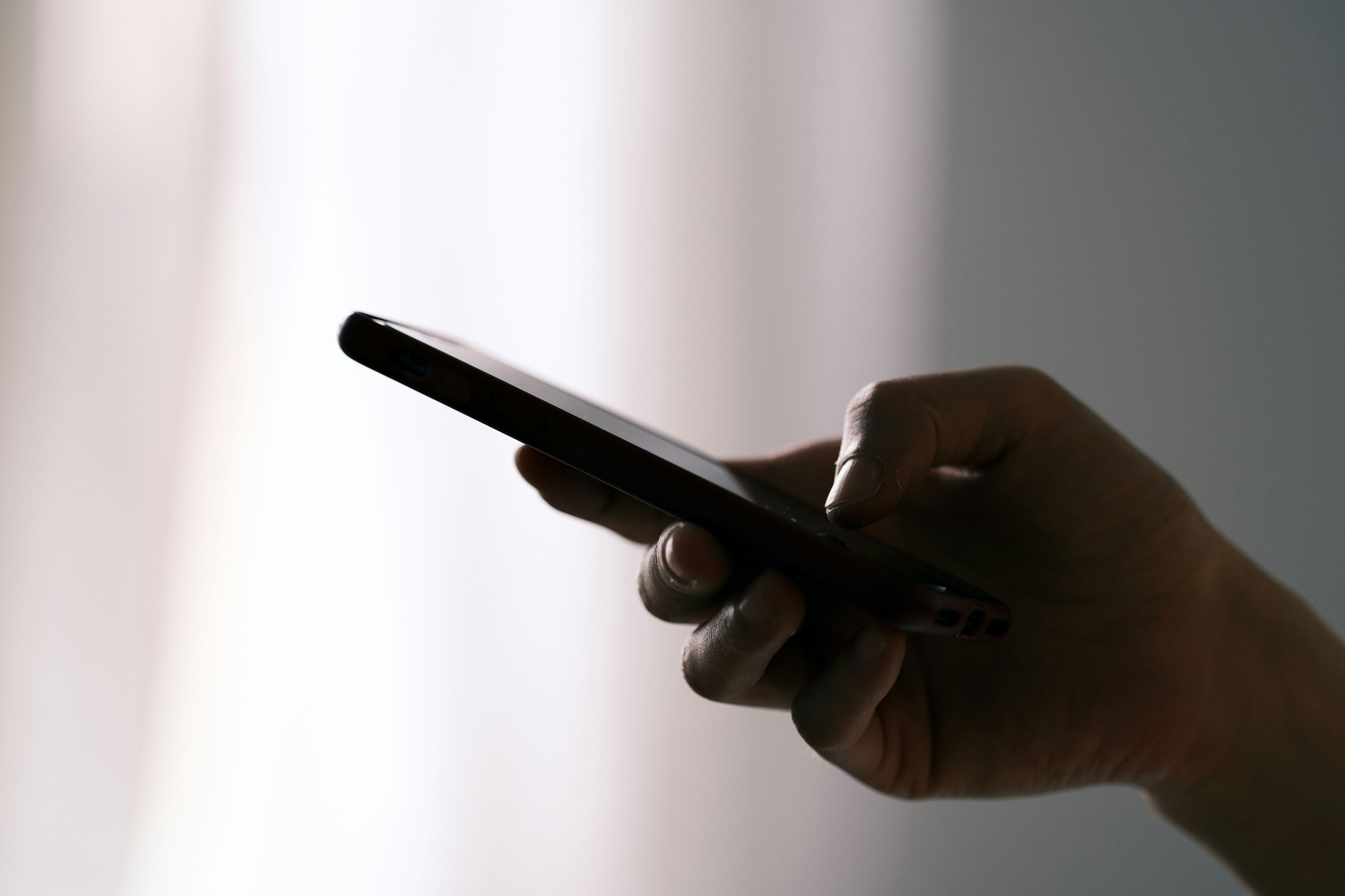 Blurred silhouette of a businessperson walking and talking on a phone beside a tiled urban building.