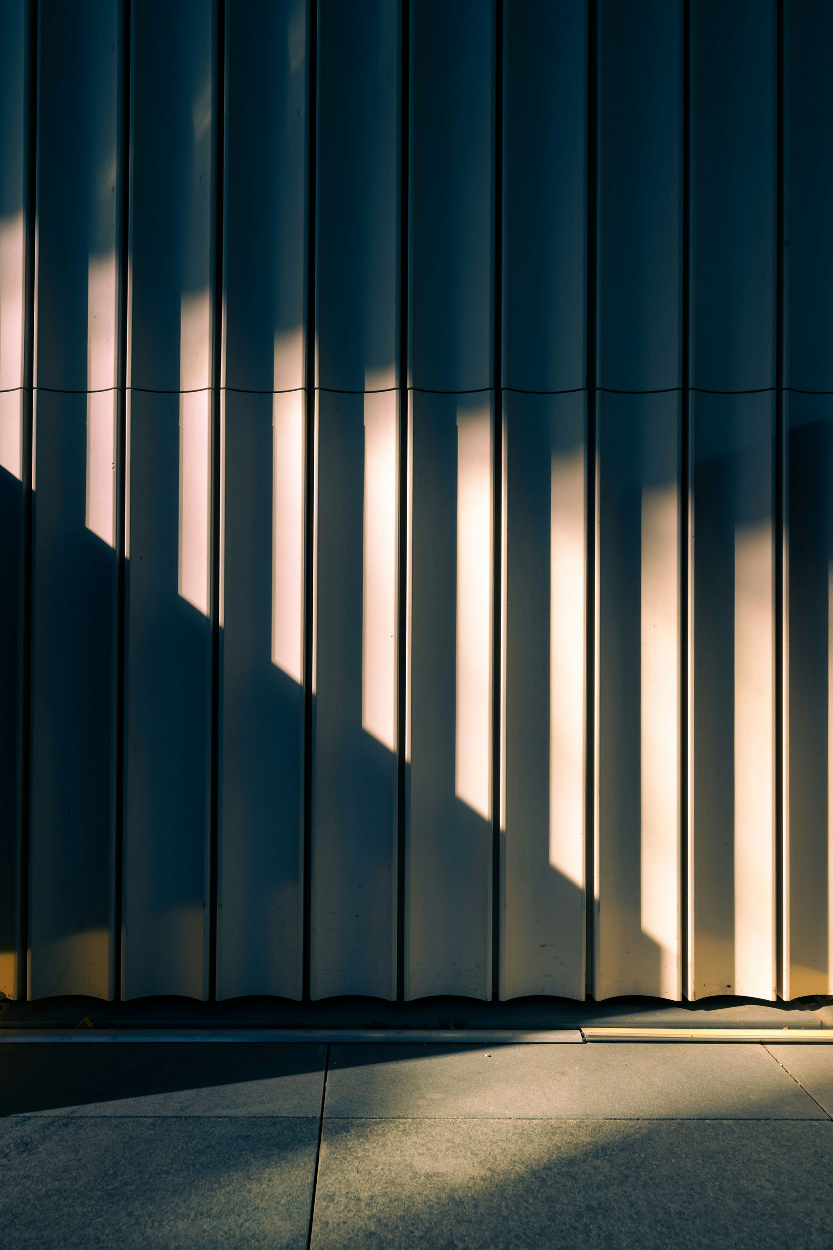 Blurred silhouette of a businessperson walking and talking on a phone beside a tiled urban building.