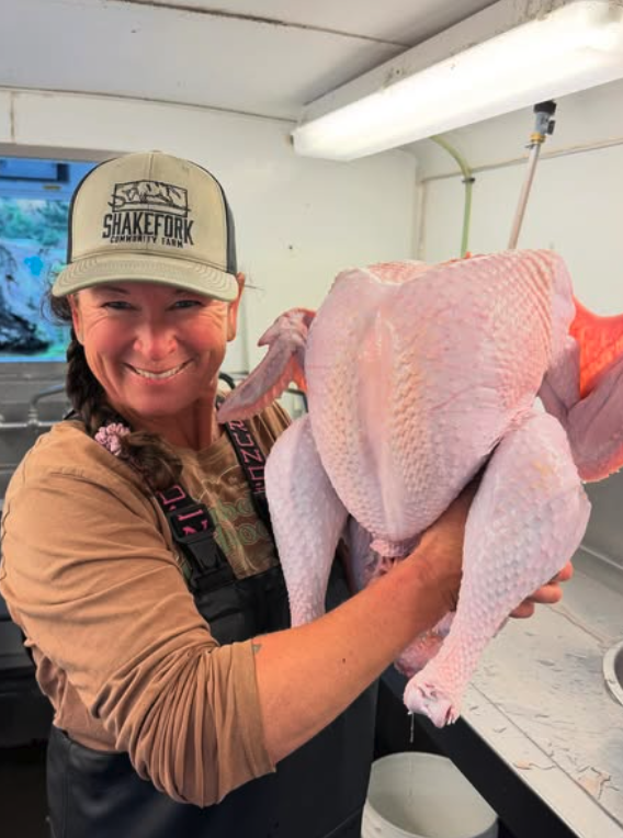 Melanie in a Shakefork cap holding a dressed pasture-raised turkey in the processing room