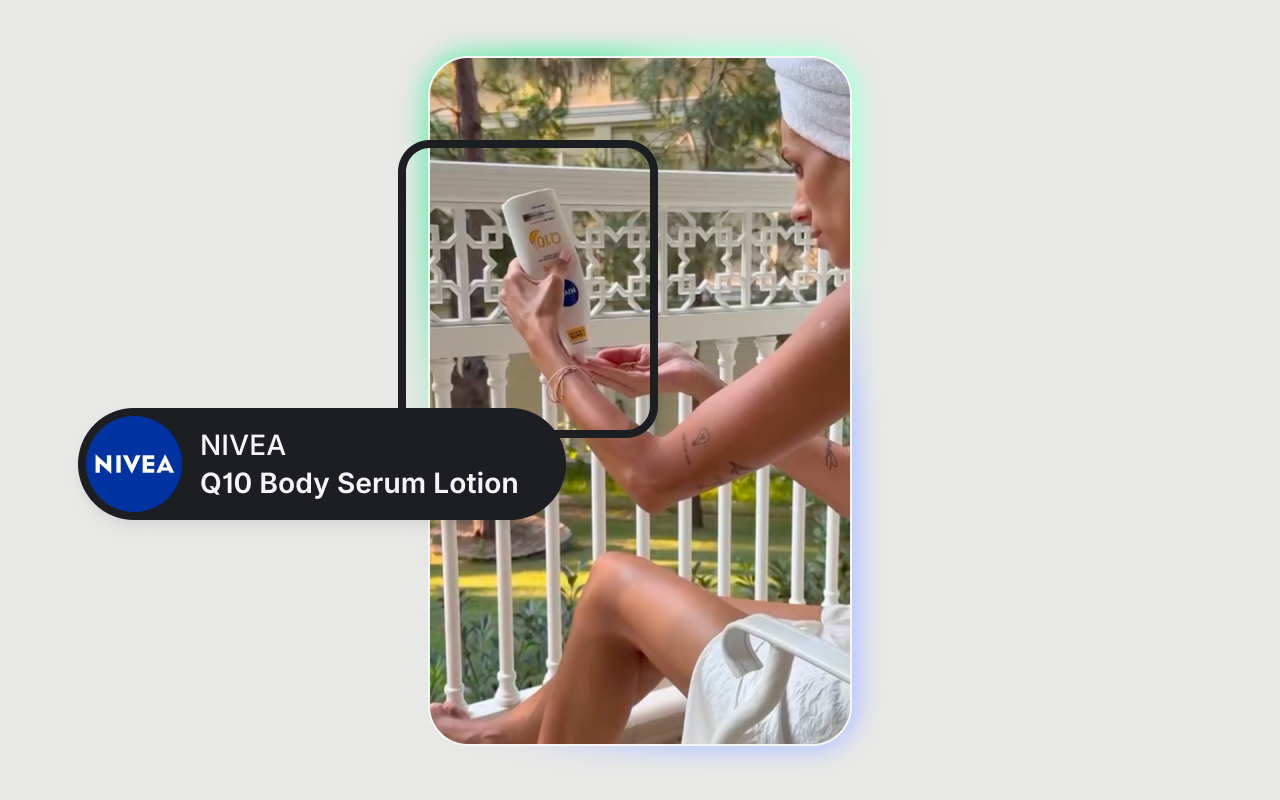 Person with a towel wrapped around their head applying NIVEA Q10 Body Serum Lotion on their arm while sitting on a balcony.