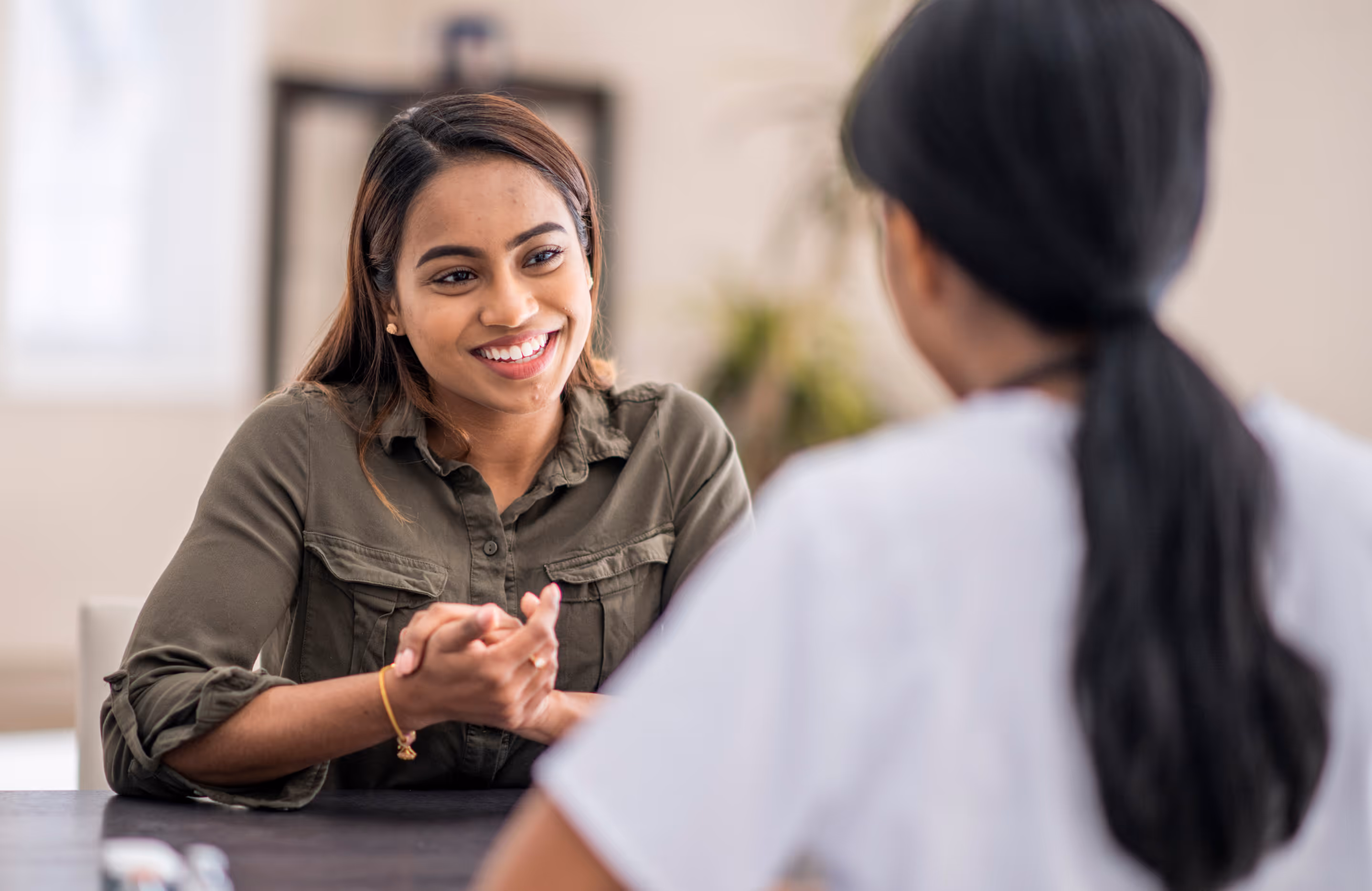 Smiling woman in olive green shirt engaged in a friendly conversation with a healthcare professional.
