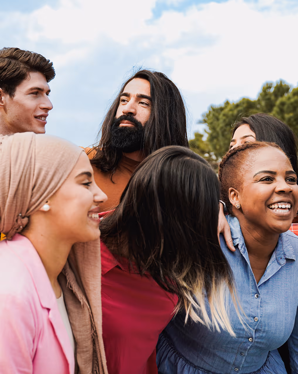 Group of diverse friends standing outdoors smiling and talking together under a blue sky.