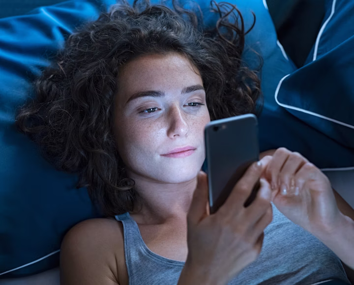 A woman lying awake in bed at night, looking at her phone