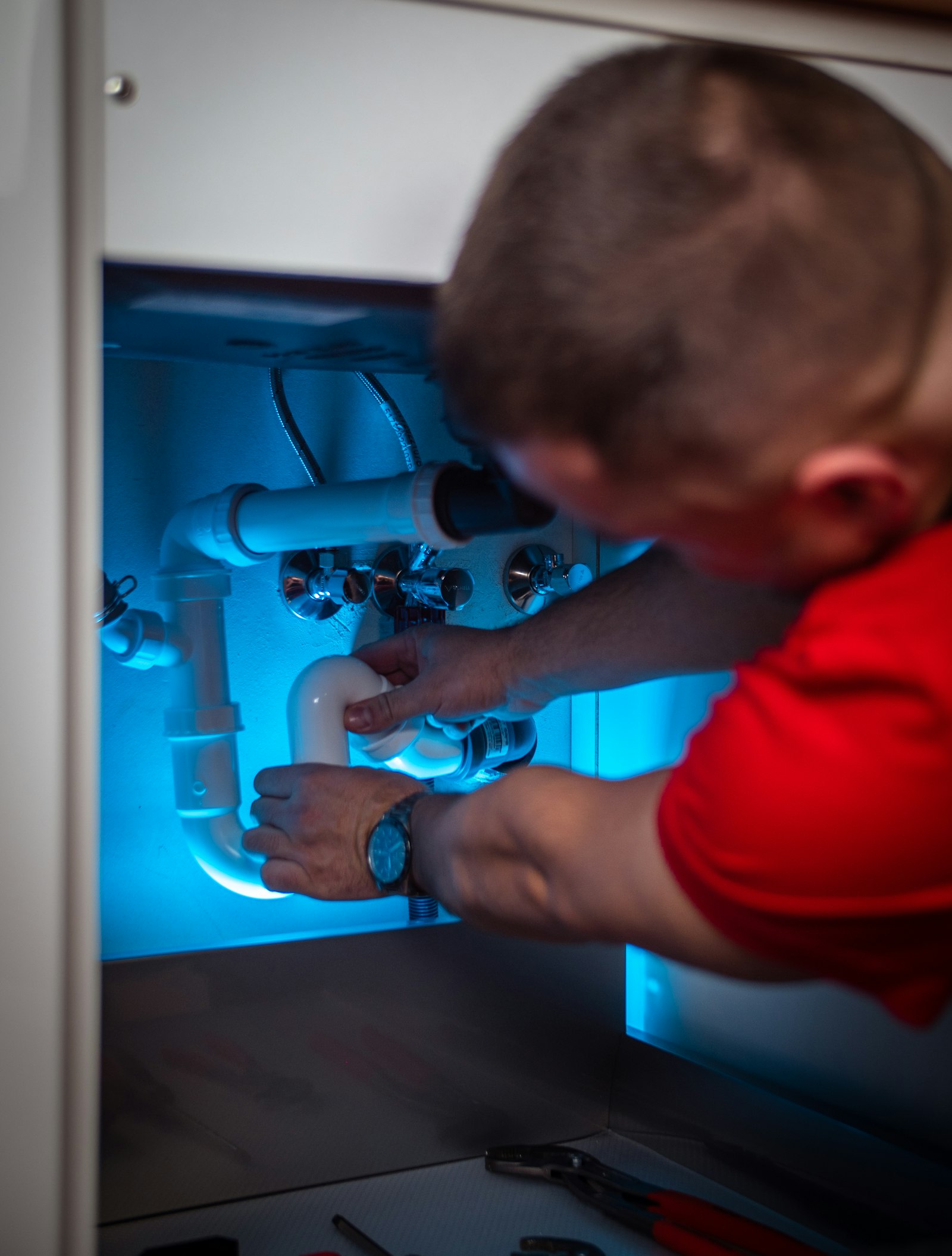 Technician repairing a leaking pipe under a sink
