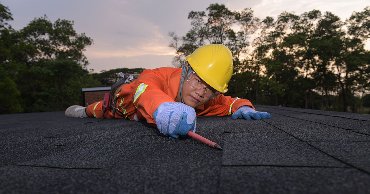 Roofing contractor in safety gear installing asphalt shingles on a Kingsport home roof at dusk