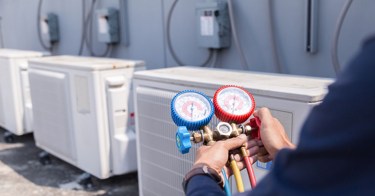 HVAC technician checking refrigerant with manifold gauges on outdoor condenser units in Morristown