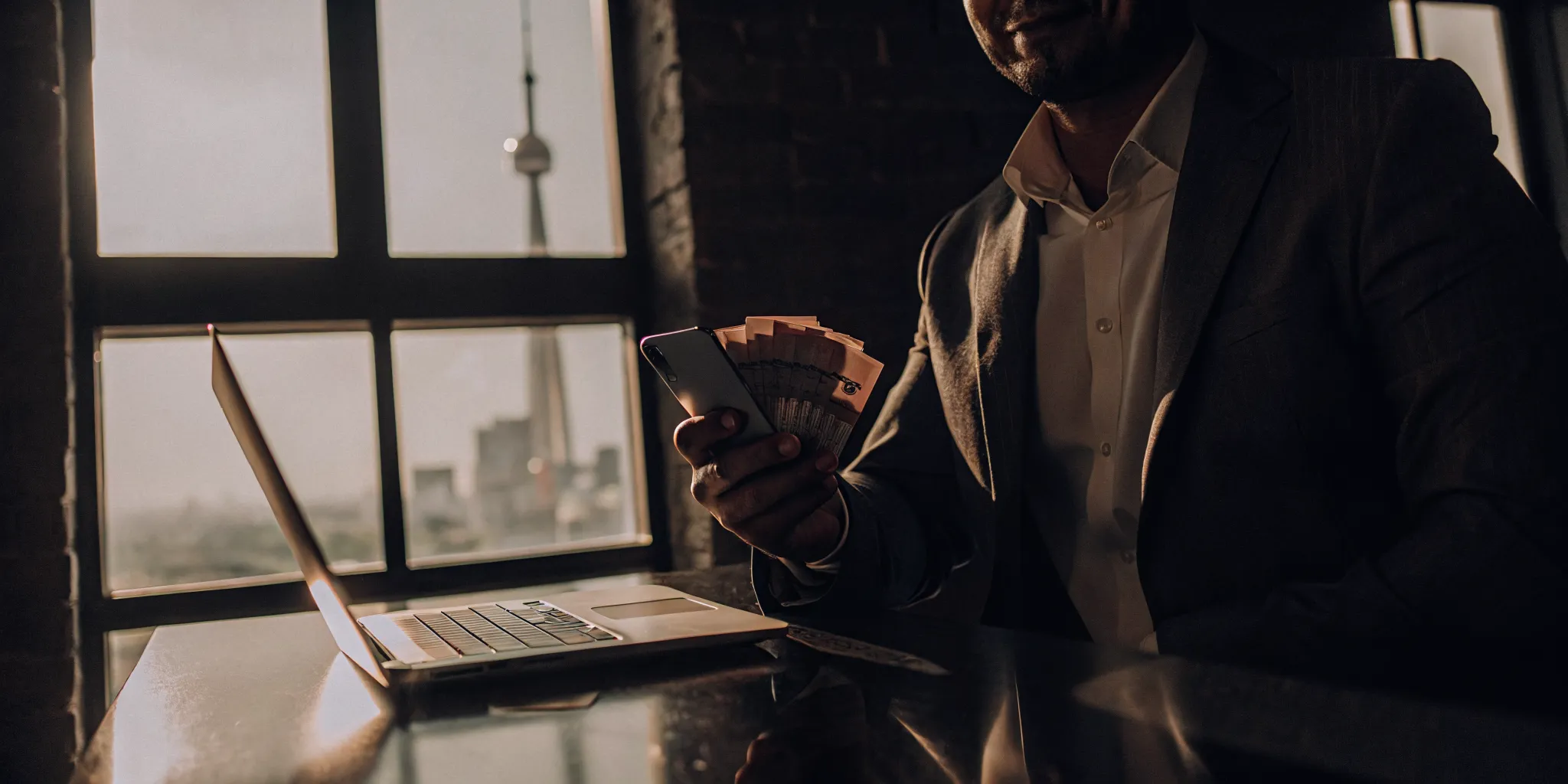 Man holding cash and using a laptop to research the best instant loans in Canada.