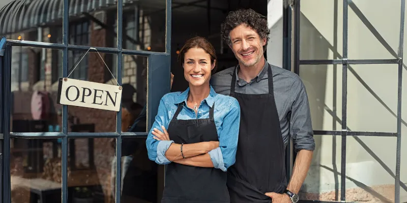 Small business partners smiling in front of their cafe after overcoming seasonal fluctuations