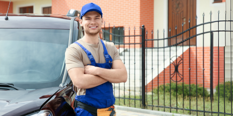 Electrician leans against a car while smiling