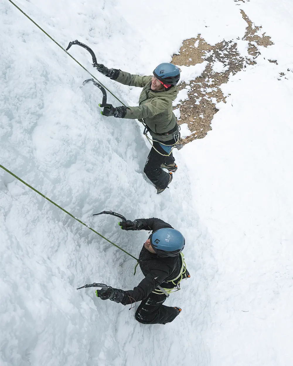 Two climbers wearing helmets and winter gear ice climbing on a frozen waterfall