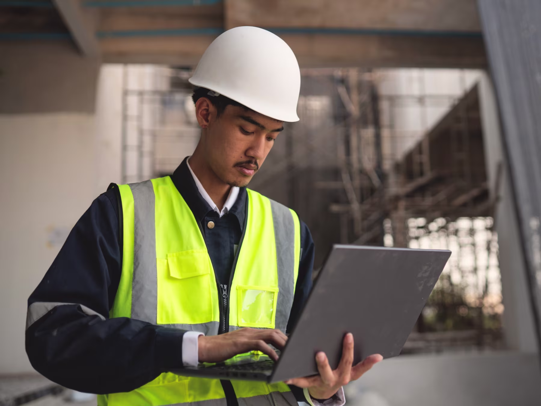 Construction project manager in a hard hat reviewing site records on a laptop