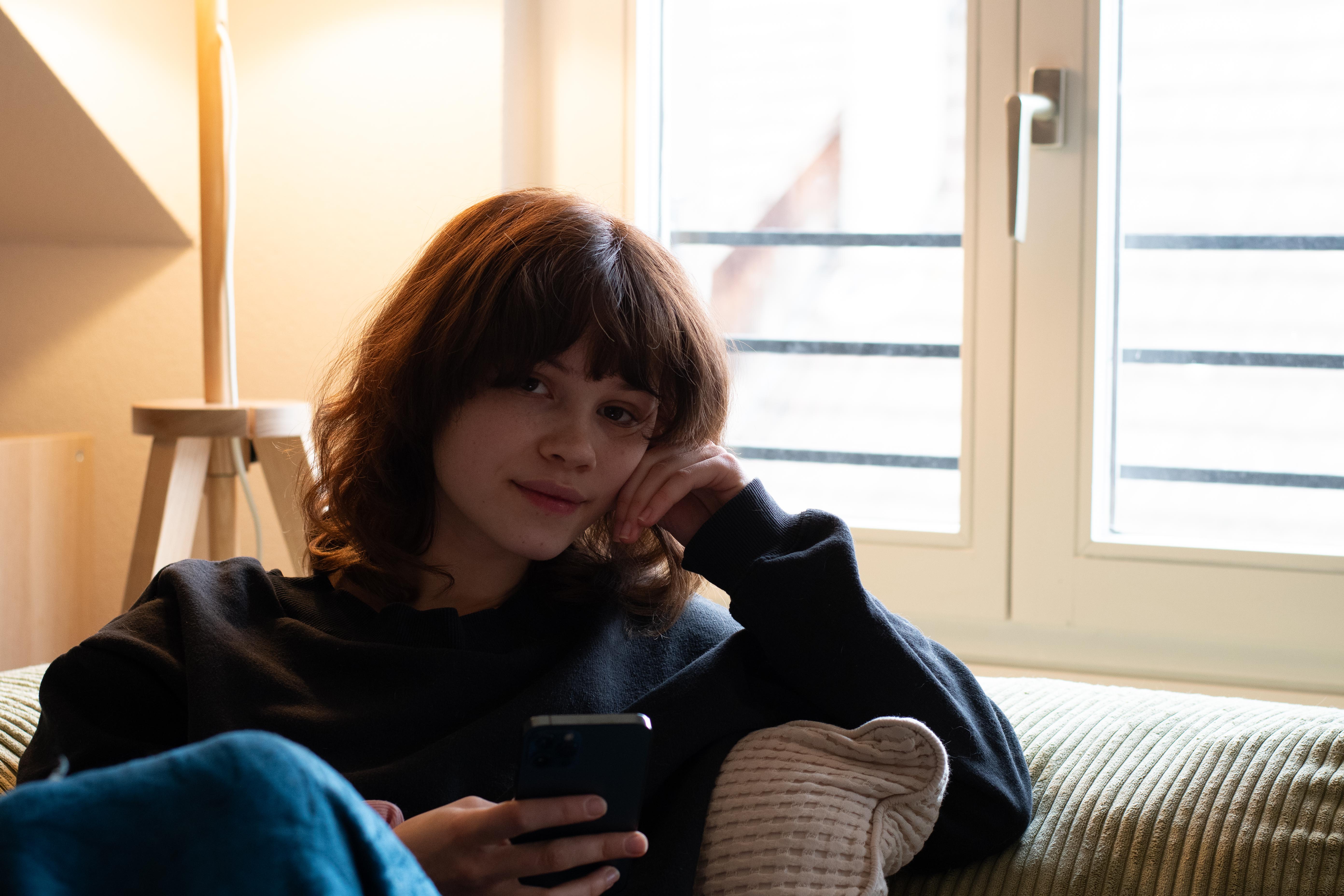 Girl looking at you, sitting on a sofa.