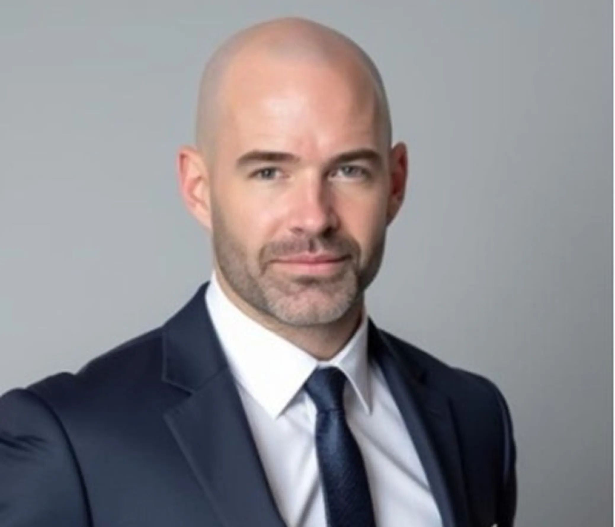Portrait of a bald man with a trimmed beard wearing a navy suit, white shirt, and dark tie.