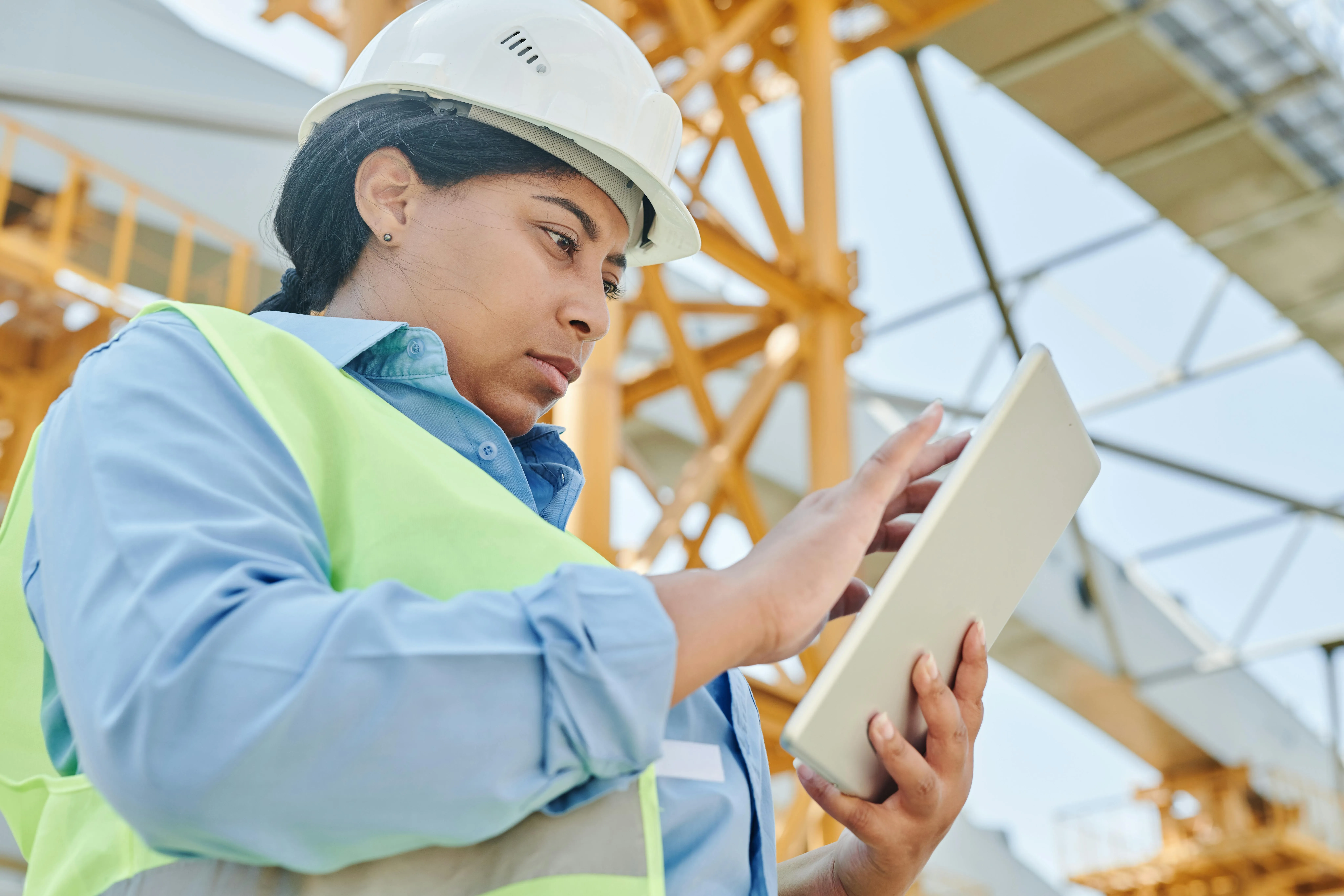 A female engineer in workwear checks her tablet on a construction site, highlighting modern engineering practices.