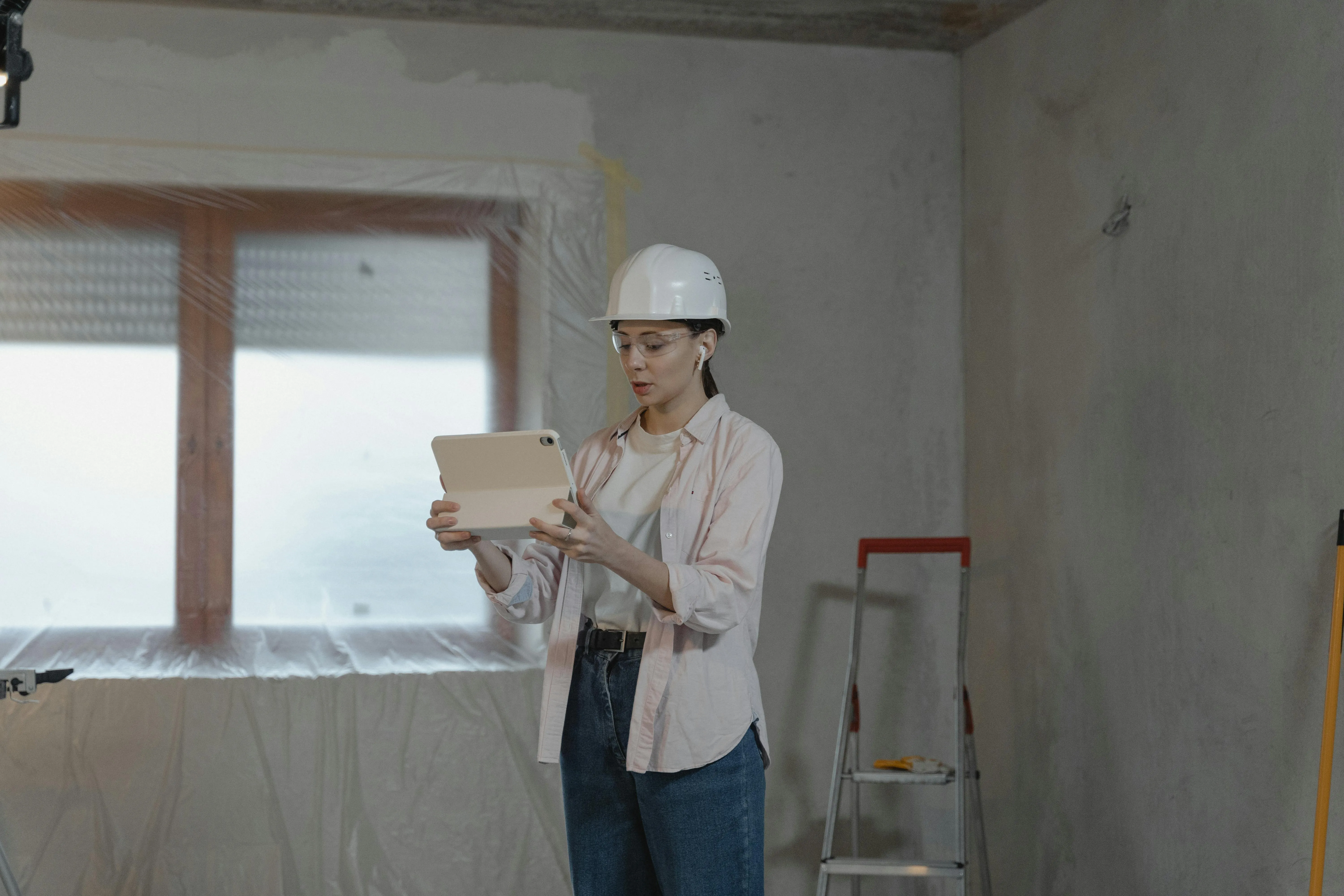Woman in hard hat using tablet for construction project in unfinished interior.