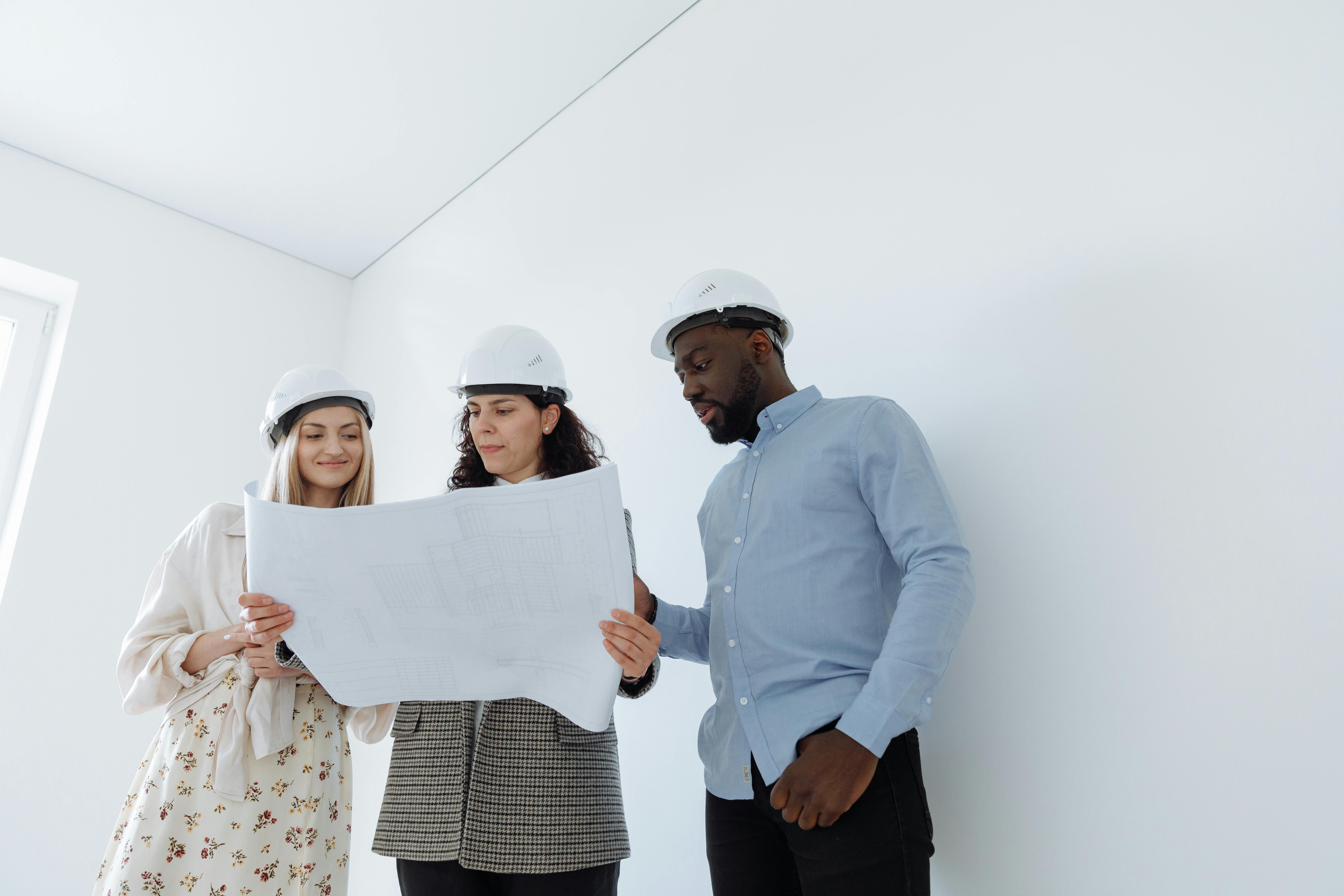 Group of professionals in hard hats examining construction blueprints indoors.