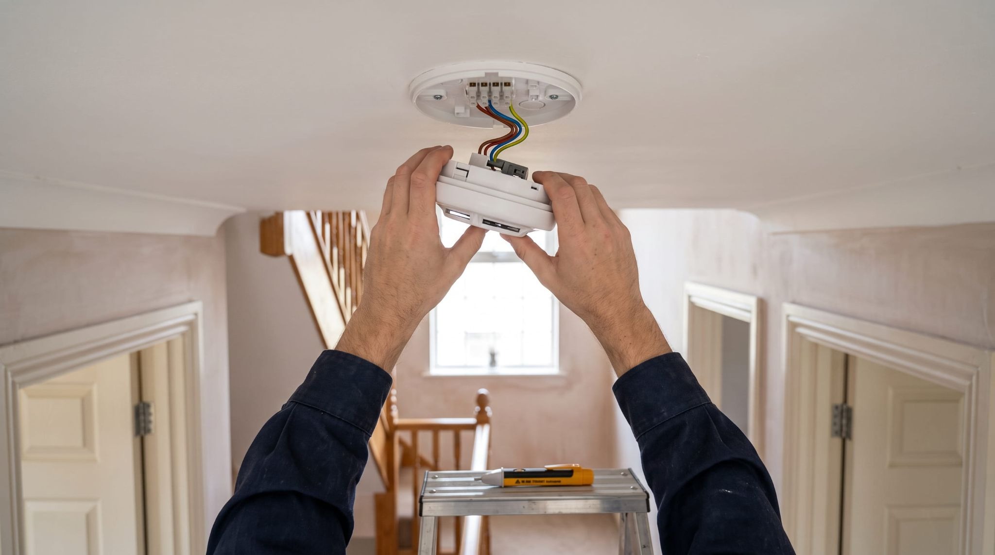 Electrician removing a wired smoke alarm head from its ceiling base to fix beeping