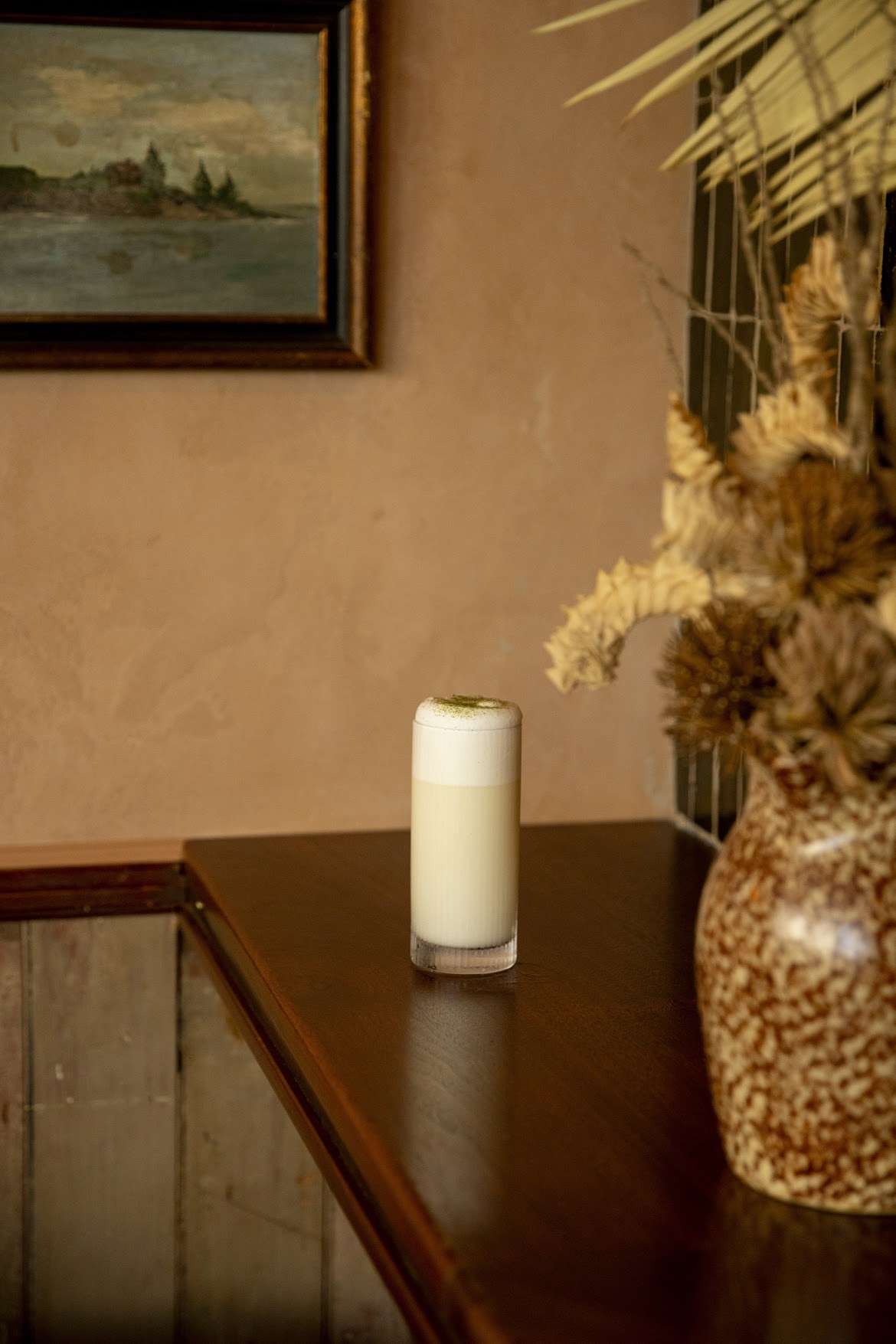 Rectangular wall display with various vintage vessels, above a piece of artwork of a vintage production site. Wooden booths with golde