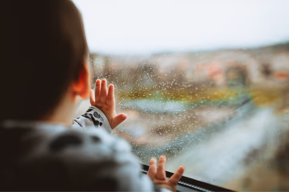 Young boy looking out rainy window