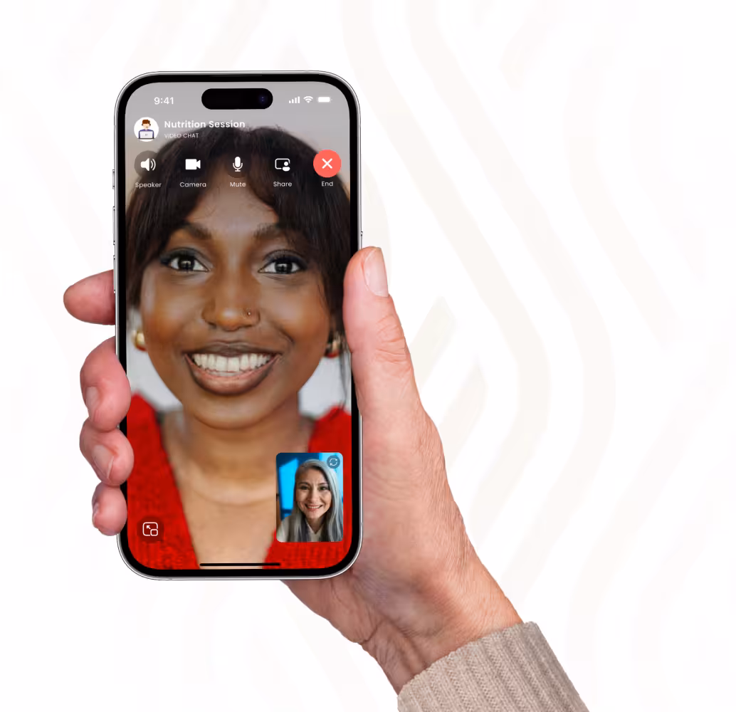 Hand holding smartphone showing a video chat with a smiling woman wearing red and a smaller inset image of another smiling woman with gray hair.