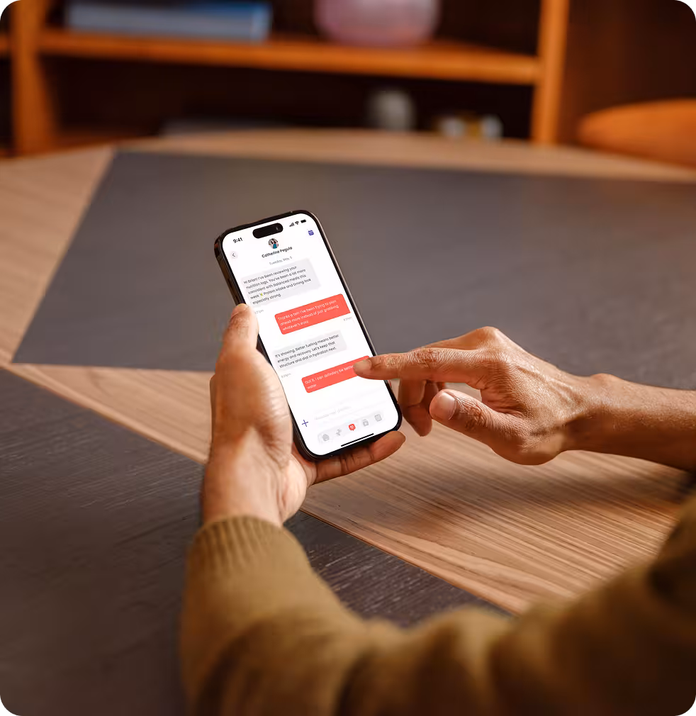Person holding a smartphone and engaging in a text conversation on a messaging app at a wooden table.