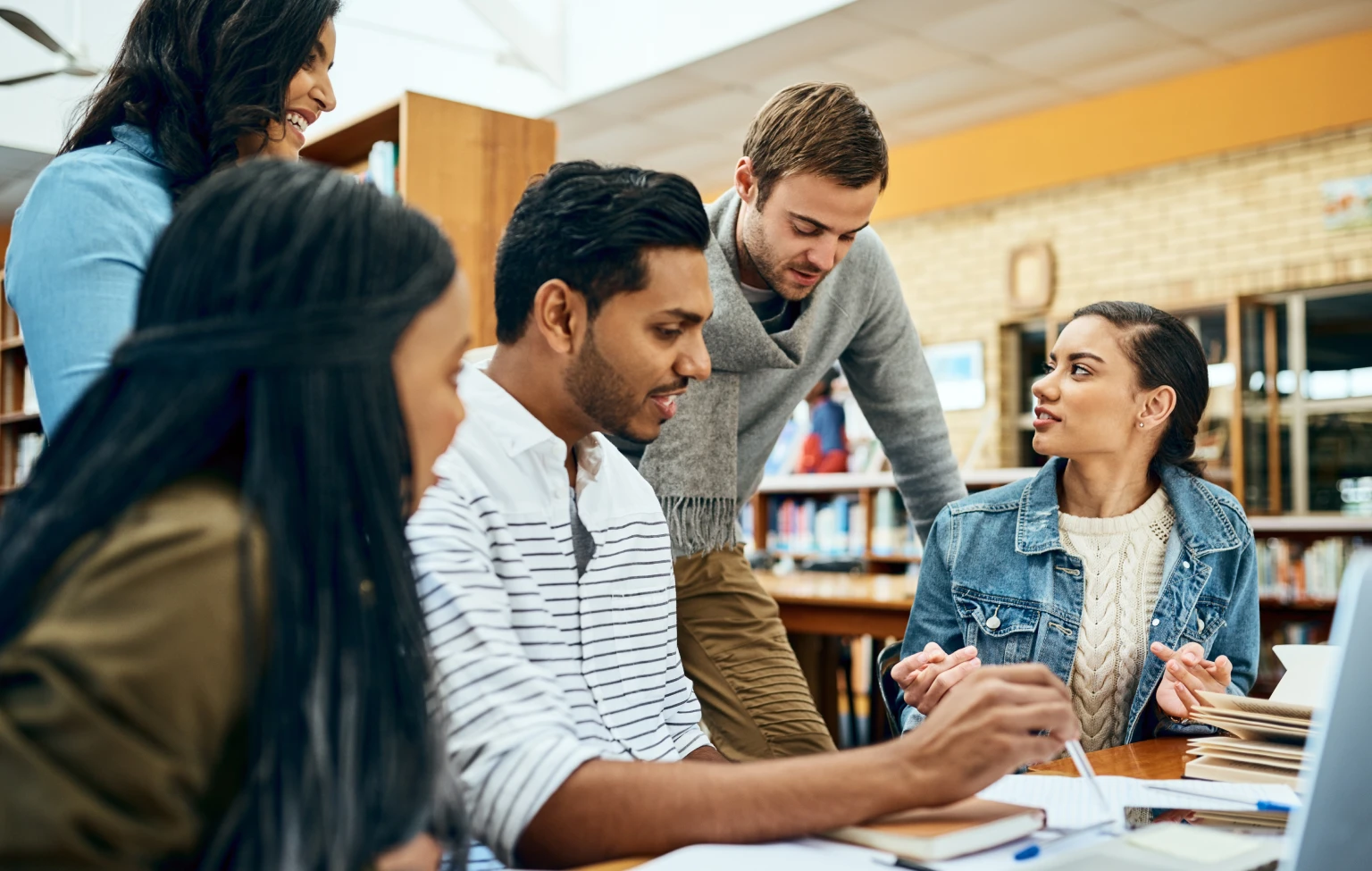 Five graduate students collaborating at a library table, discussing notes and books during a group study session.
