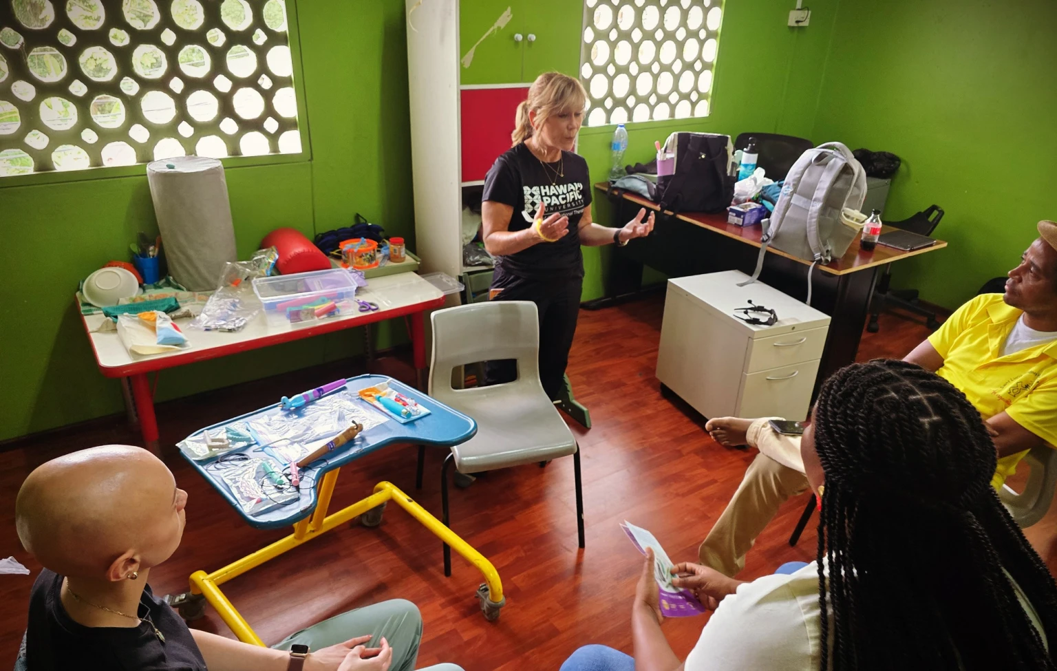 HPU OTD faculty member leads a hands-on training session with local educators in St. Lucia, surrounded by therapy tools used during the service-learning experience.