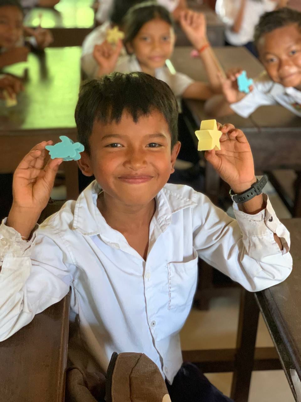 A smiling schoolboy holding up star- and animal-shaped SOAPLAY soap bars