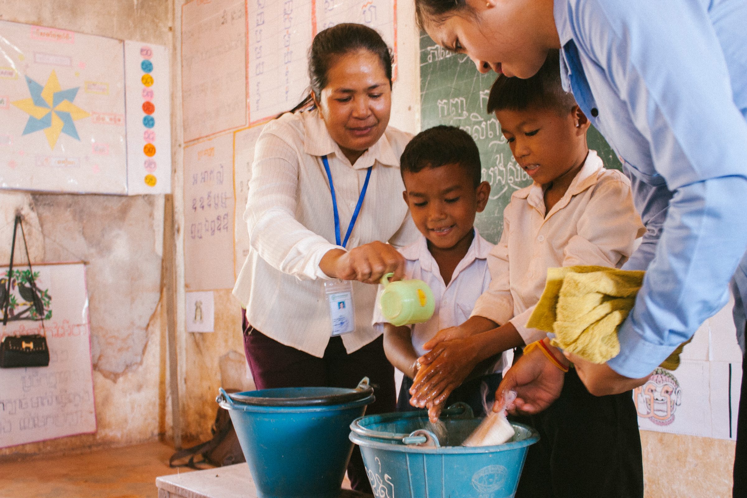 A teacher helping schoolchildren wash their hands with soap