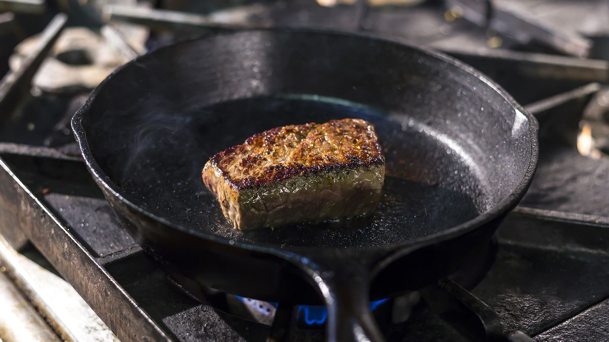 steak searing in a cast iron skillet on a gas stove burner
