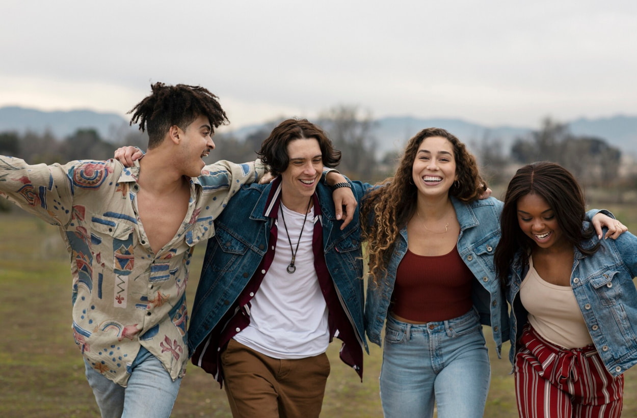 Four young people stand together in a grassy field, smiling and enjoying the outdoors. 