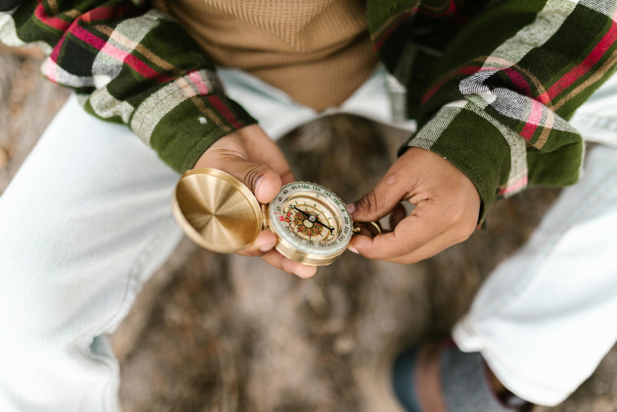 A person seated on a wooden bench, intently holding a compass in their hands, surrounded by nature.