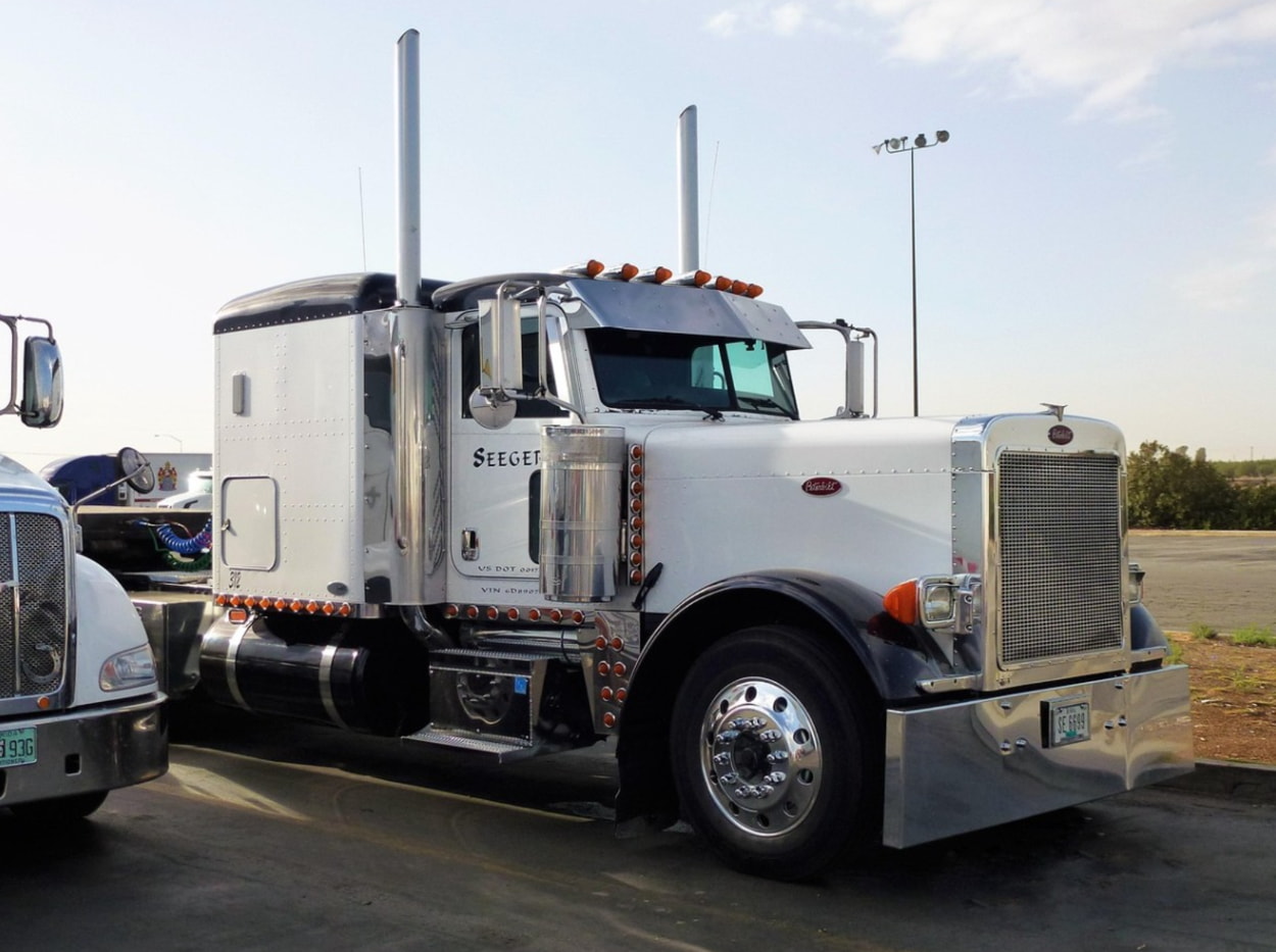 A white semi truck parked on a highway, showcasing its large trailer and distinctive cab design.  