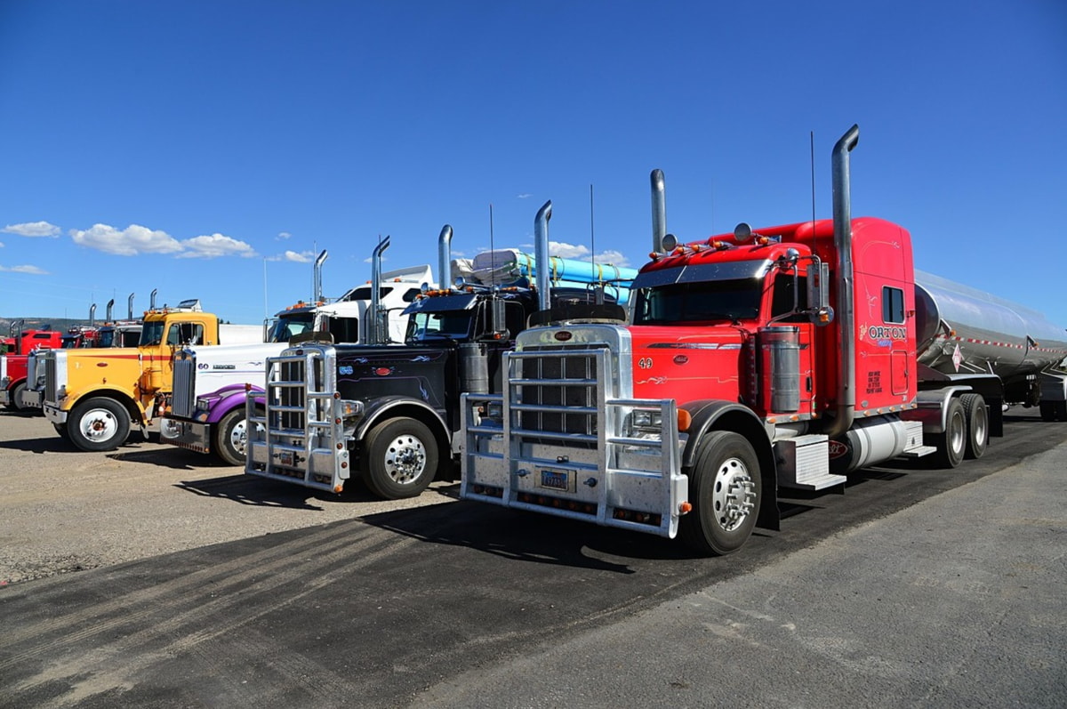 A row of semi trucks parked neatly in a spacious parking lot under clear blue skies.  