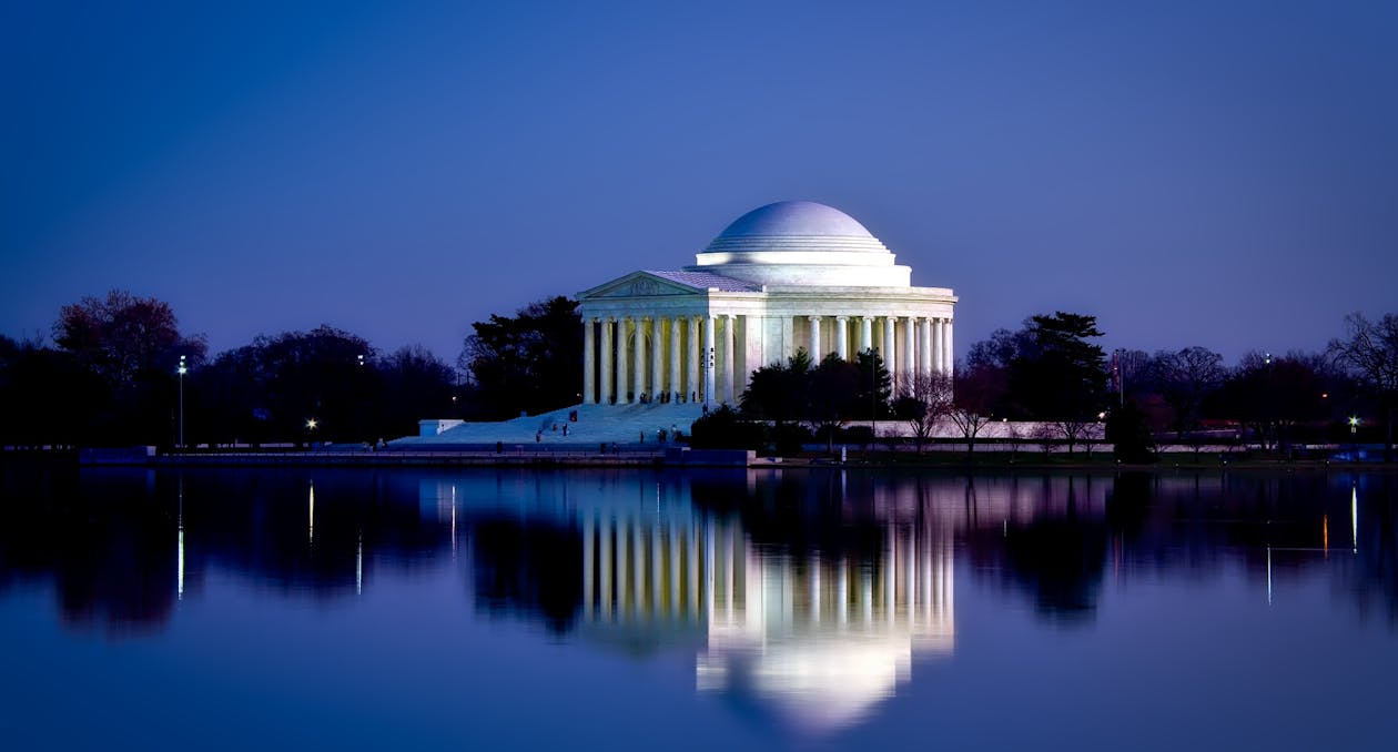 The Jefferson Memorial illuminated at night, reflected in calm water, creating a serene and picturesque scene.  