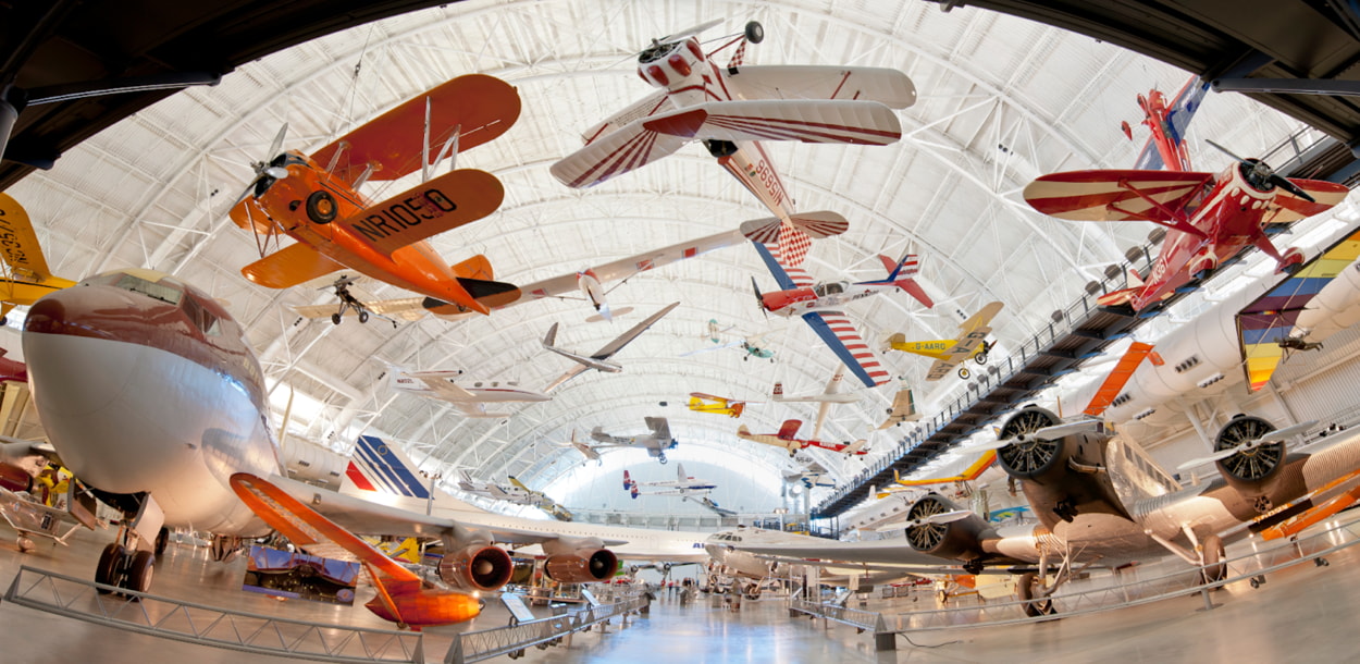 A spacious room filled with various airplanes suspended from the ceiling, showcasing aviation history and design.  