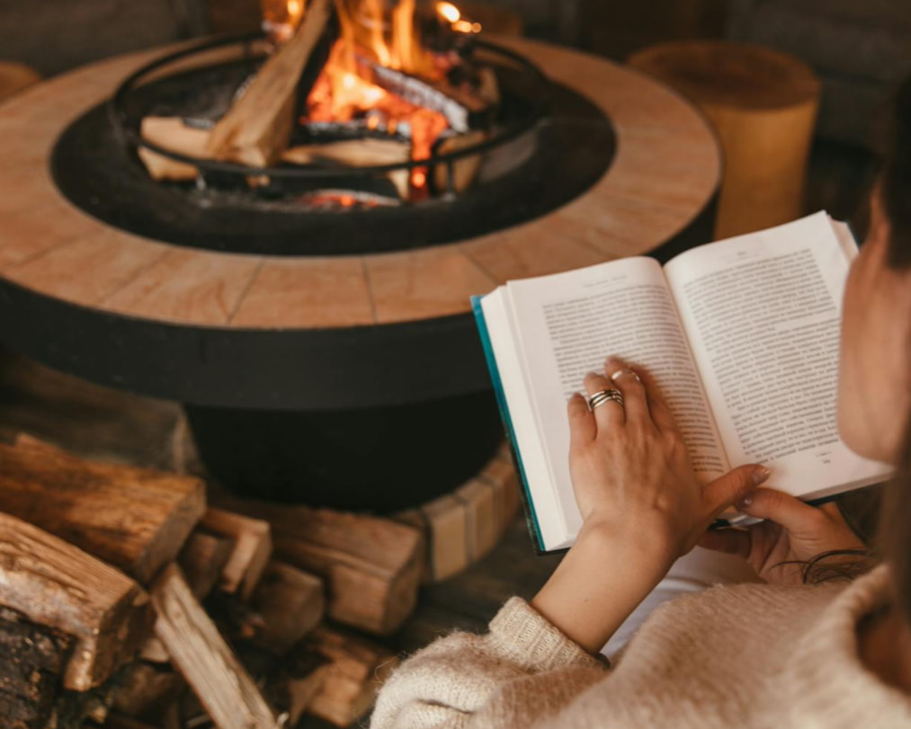 A woman reading a book while sitting comfortably by a warm fireplace, creating a cozy atmosphere.