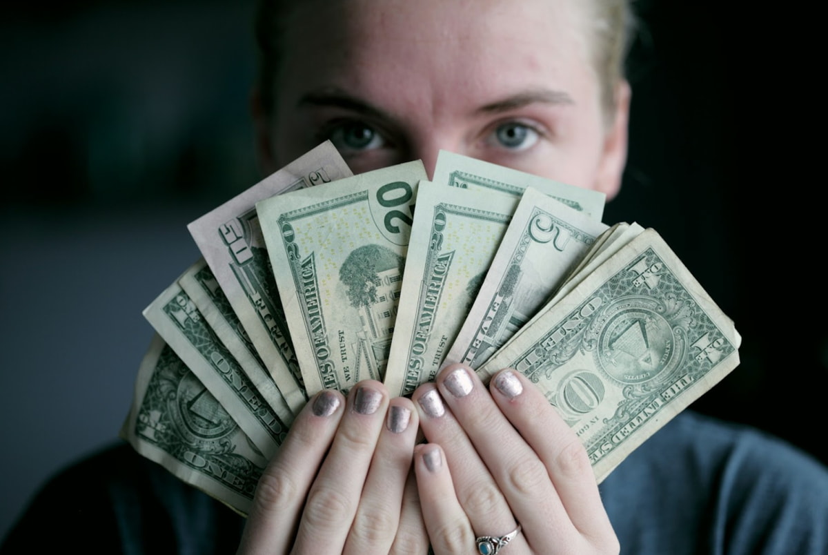 A woman holds a bundle of money in her hands, showcasing it with a confident expression.