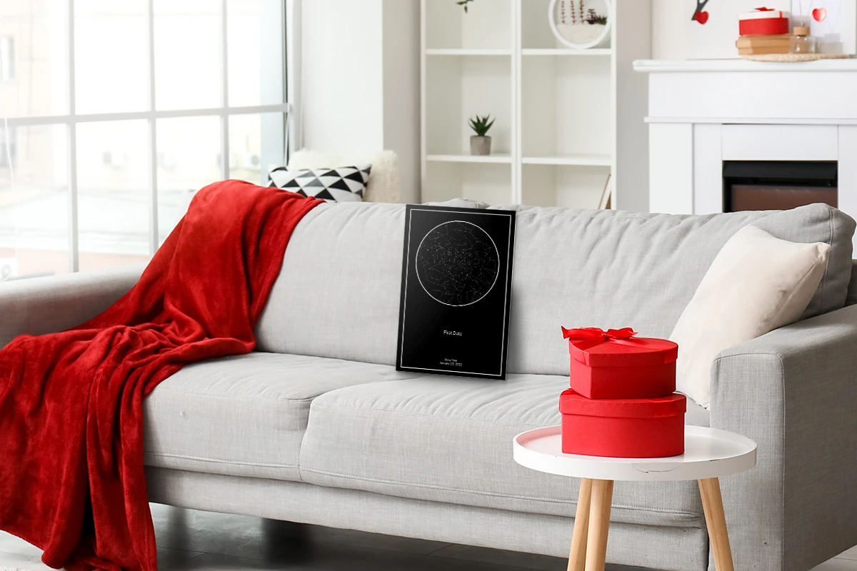 A cozy living room with a gray sofa draped in a red blanket. A star map poster rests on the sofa, and red gift boxes sit on a nearby white table.