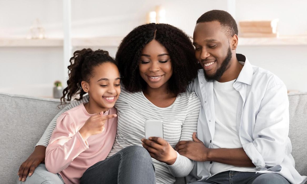 A family gathered together, smiling while using a smartphone to share photos or messages.