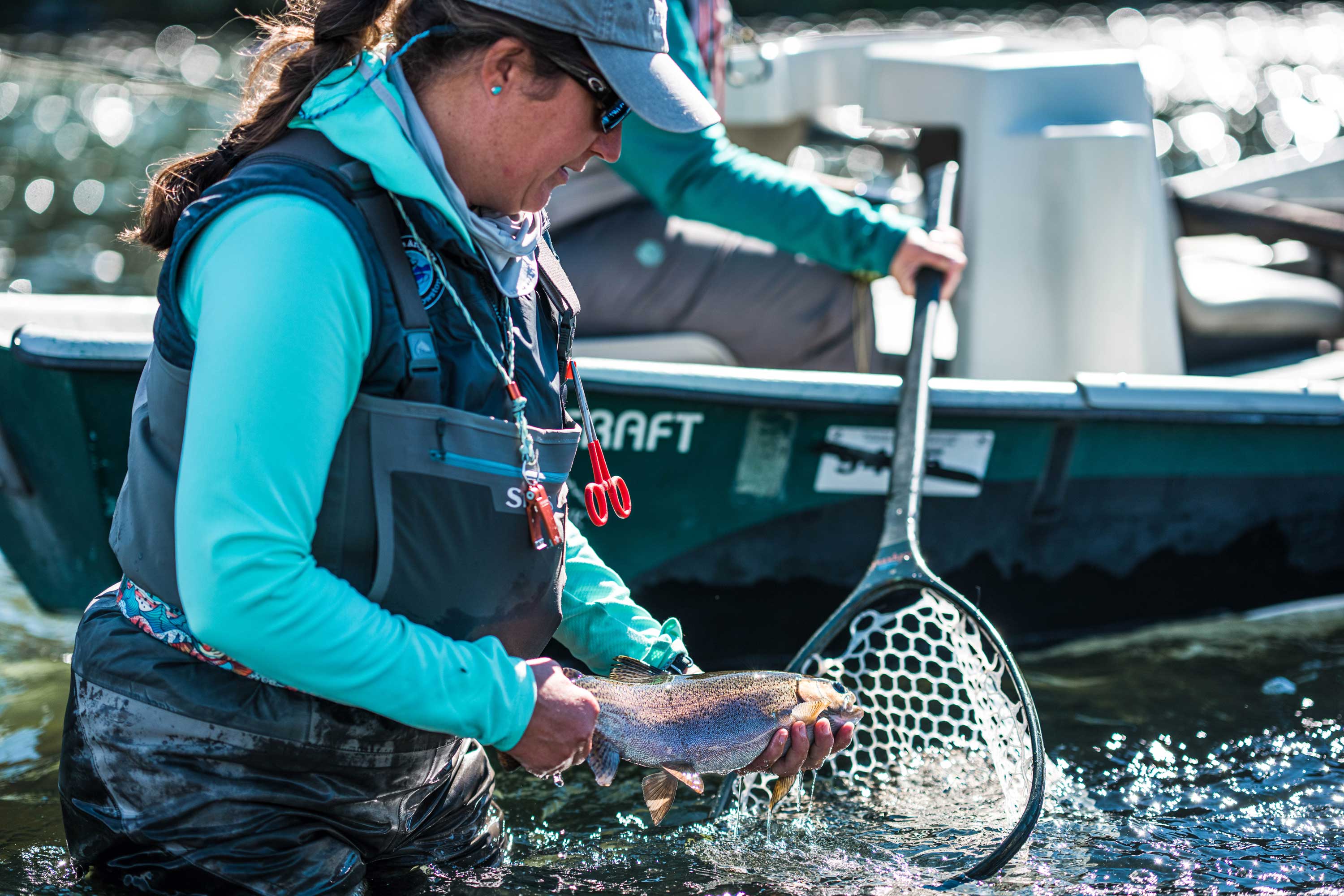 Woman wading through water holding fish about to put it in a net