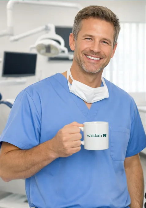 Smiling male dentist in blue scrubs holding a white mug with 'wisdom' text and a tooth icon in a dental office.