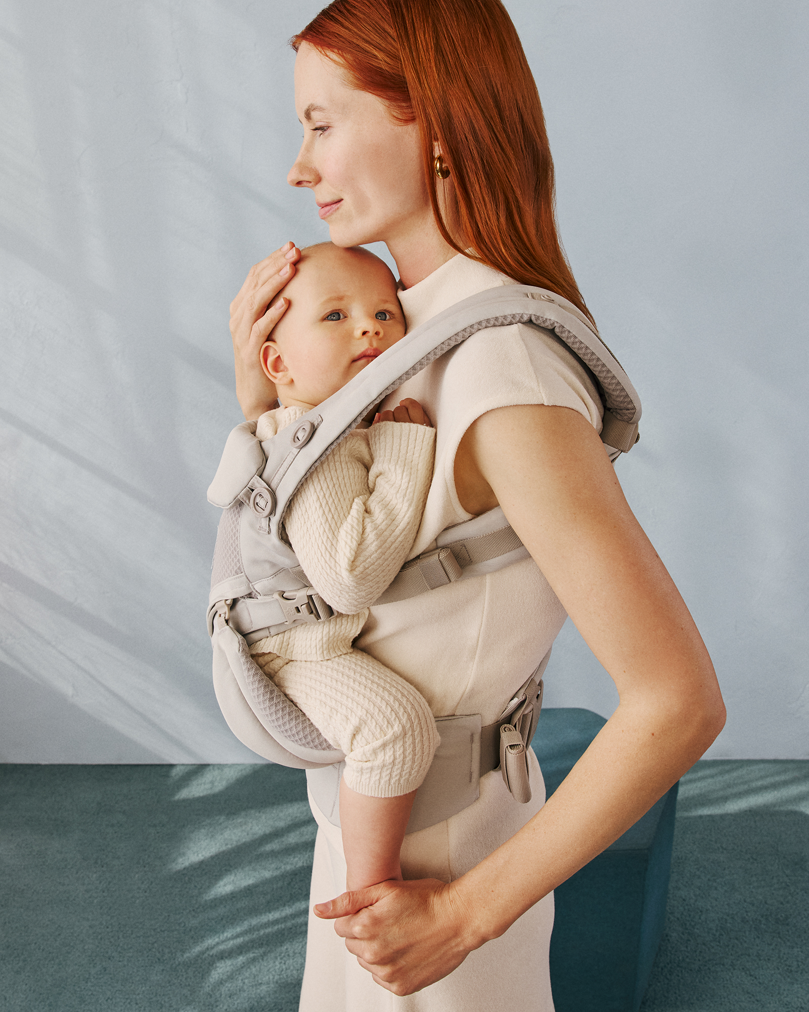 Parent outdoors carrying a baby in a beige Ergobaby mesh carrier
