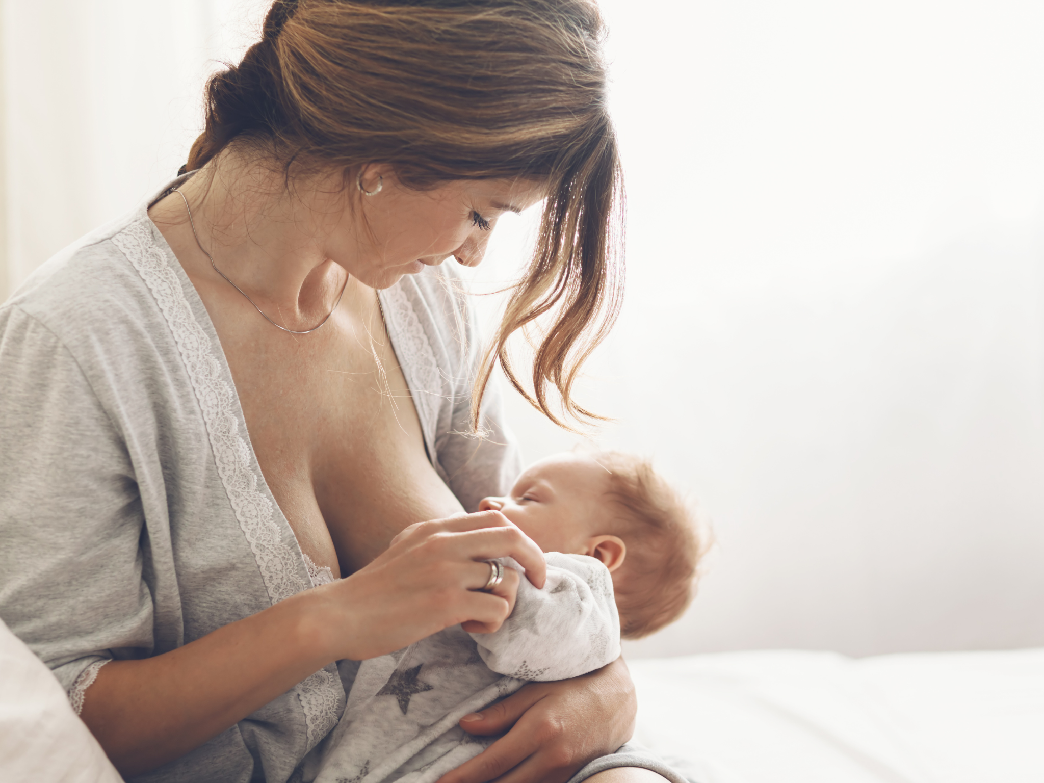 Close-up of a newborn baby breastfeeding, held gently by mother