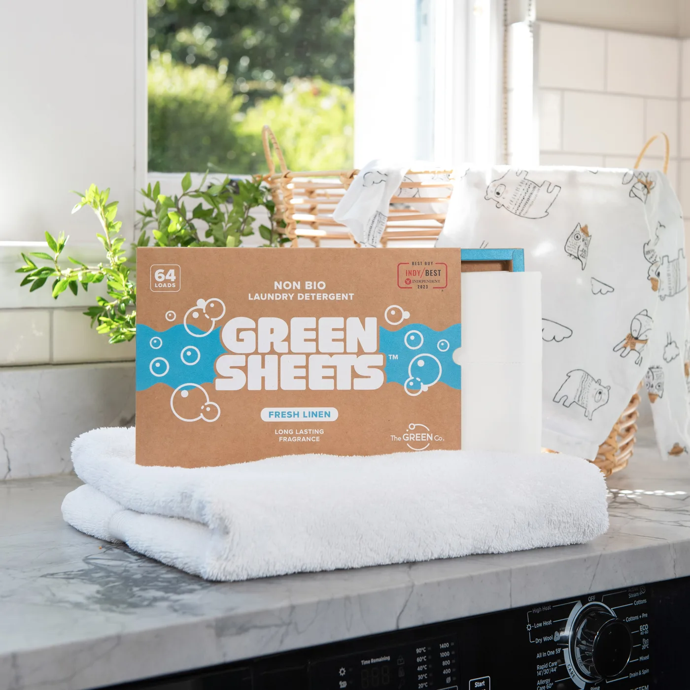 A box of Green Sheets non-bio laundry detergent sheets on a folded white towel beside a basket of baby muslins