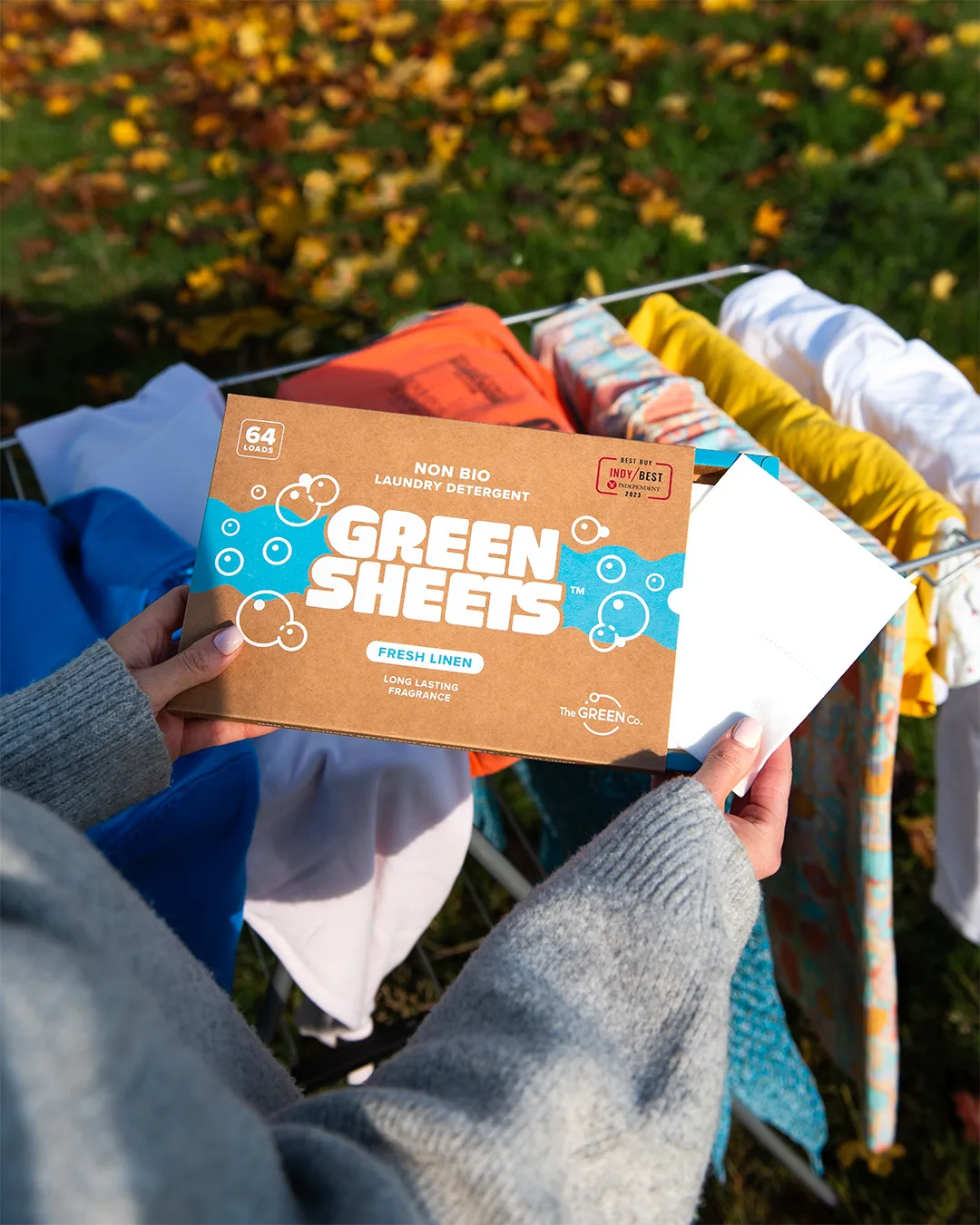Holding a box of Green Sheets over a clothes airer of drying washing outdoors