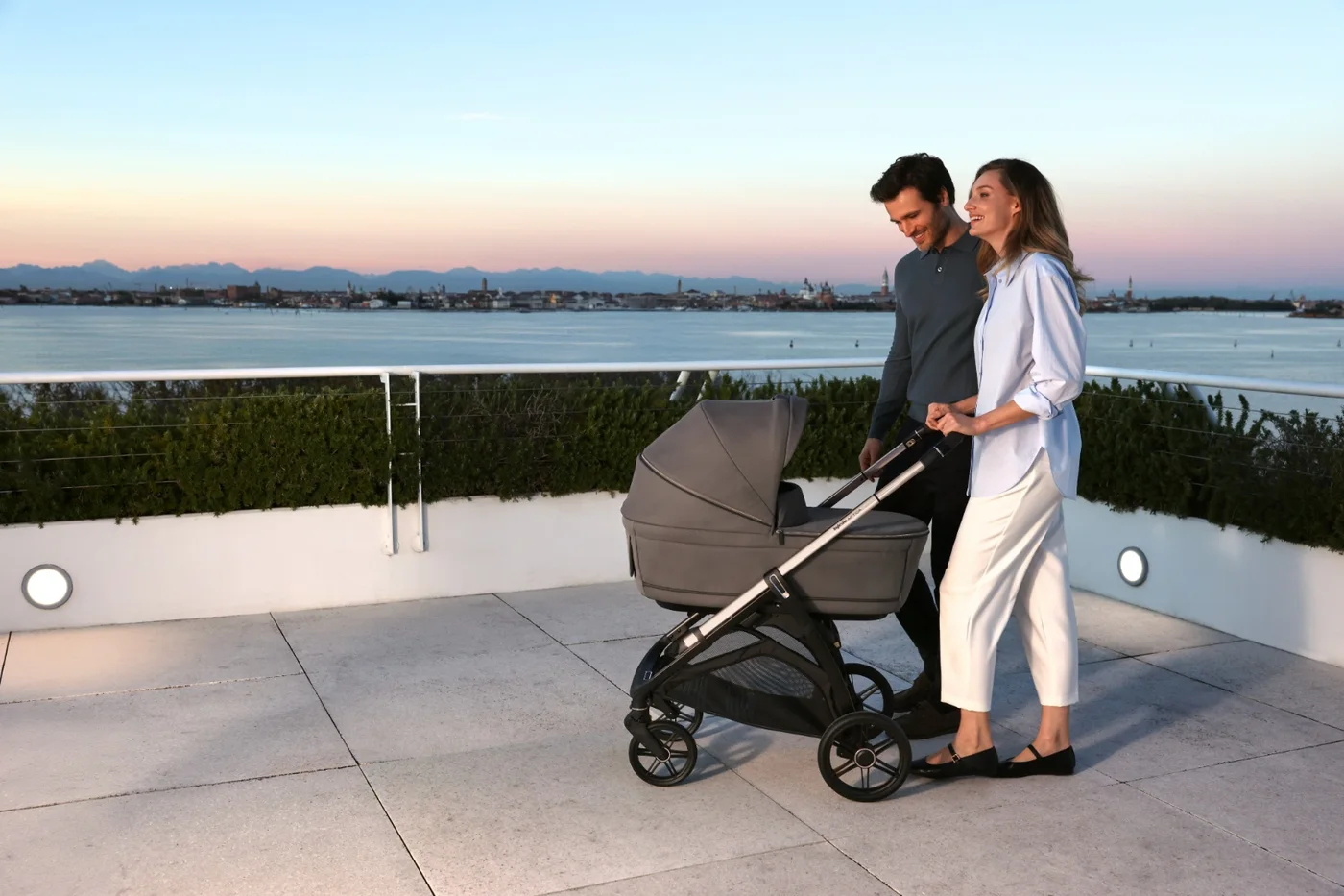 A couple walking with an Inglesina travel system on a rooftop terrace at sunset