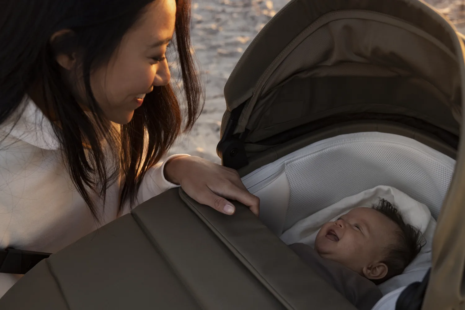 A mum leaning over her baby asleep in the Thule Charm bassinet