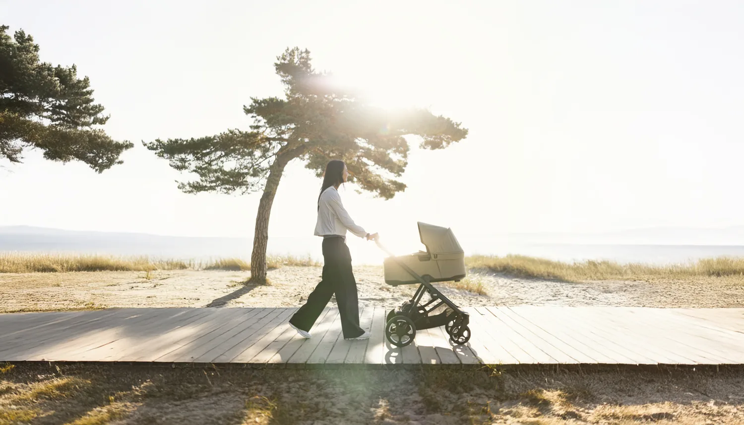 A parent pushing the Thule Charm pushchair along a sunny beach path